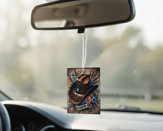 Car air freshener with a cowboy hat design hanging from a car's rearview mirror.