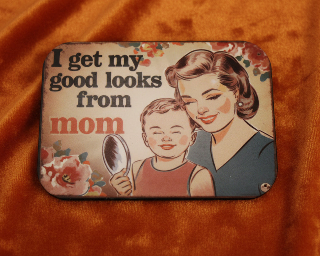 Decorative sign with a vintage-style illustration of a woman and child, and text 'I get my good looks from mom' on a beige background.